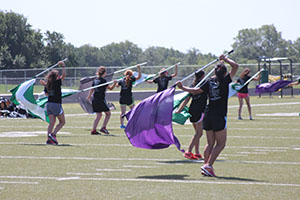 The guard girls gracefully swing their flags over their heads. 