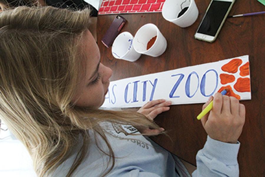 Helping out at the homecoming work day, senior Kathryn Venzon paints a sign that says “Kansas City Zoo.” This sign was included in the front entryway at the dance. 