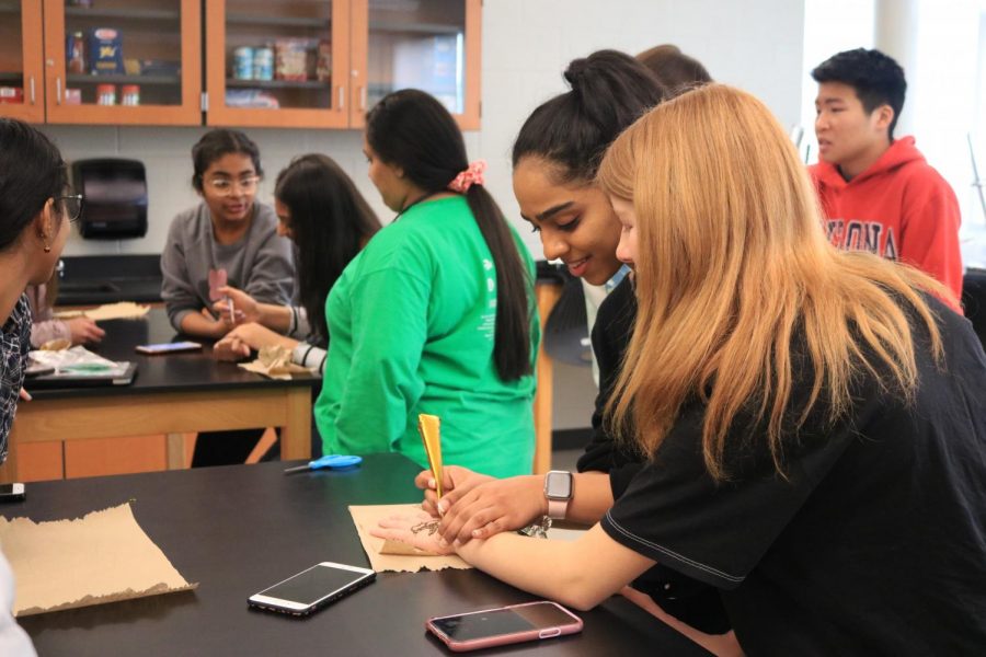 Sophomore Ellie Philips looks over as sophomore Evanna Dominic squeezes henna onto her hand. Photo by Rebecca Suku.