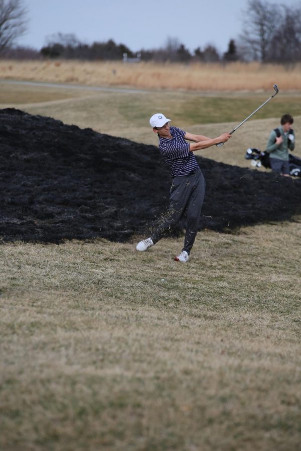 Following through, senior Justin Wingerter chips onto the green at practice on March 4. Photo by Kenna Plaster.