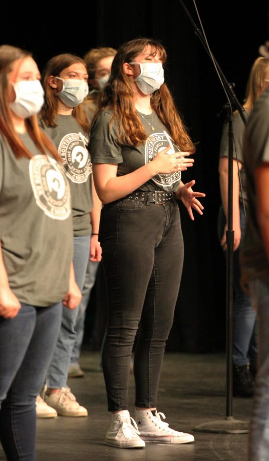 With her hands up, junior Carolyn Brotherson sings passionately on stage. 