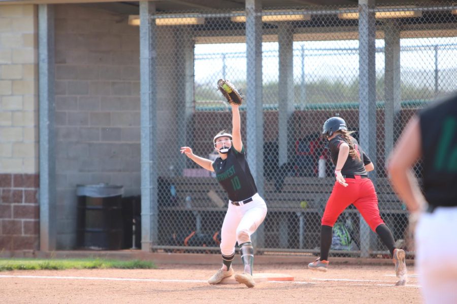 Arm raised high, sophomore Riley Baber catches a throw made to first in order to get an out on May 17.