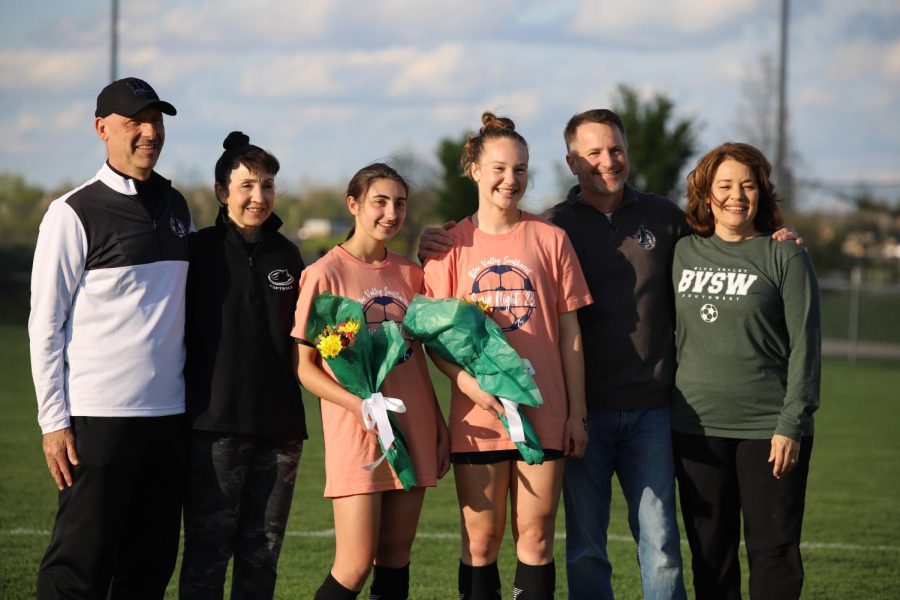 Flowers in hand, seniors Regan Cannon and Lena Palmieri pose for a photo with their parents during the Senior Night celebration on April 20. After the game, the seniors handed out treats to their teammates.