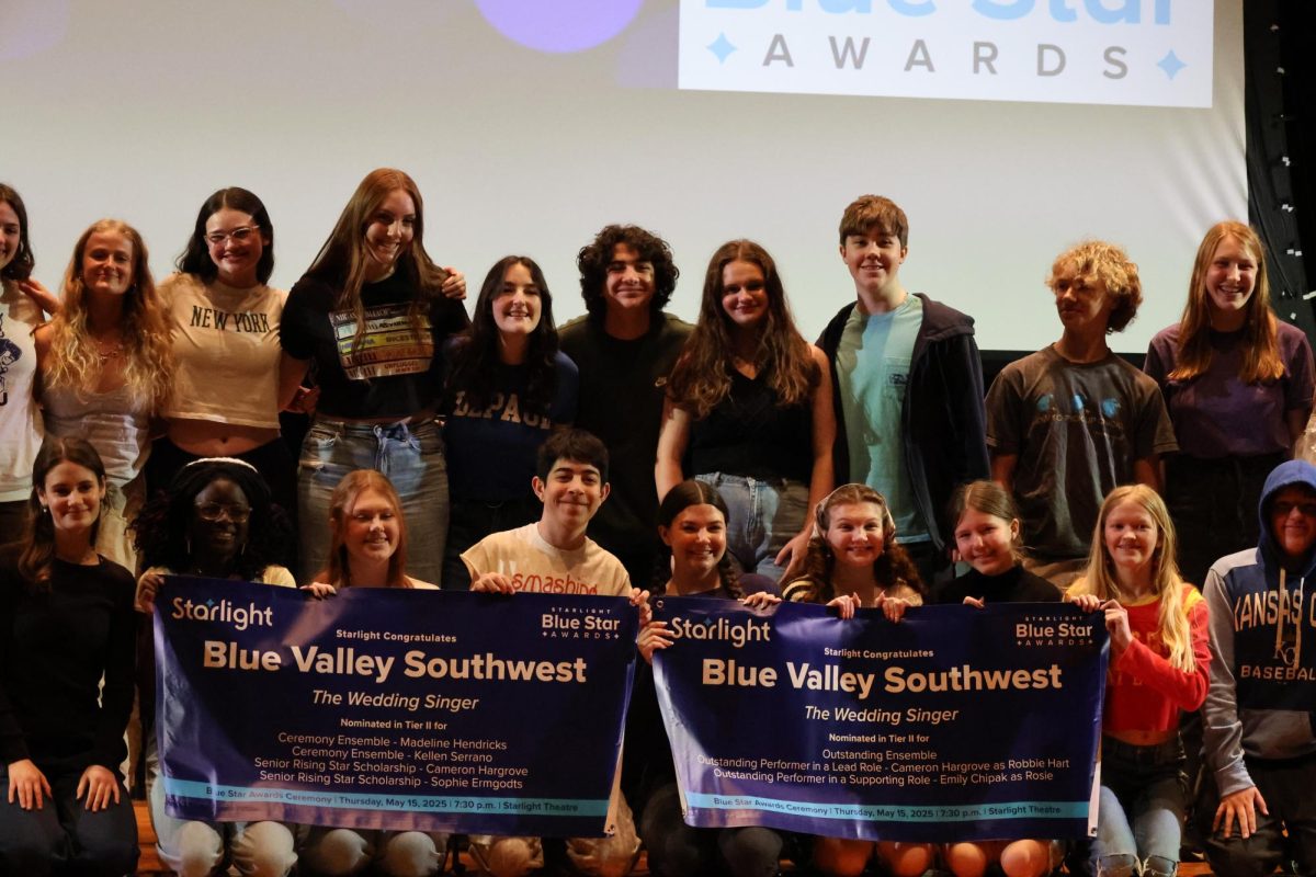 The cast holds up their awards on the stage and are smiling for a picture. 