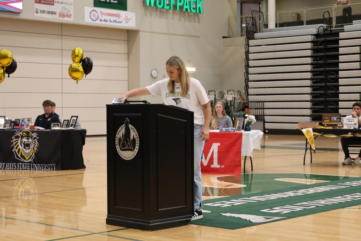 Arm reaching, senior Karter Skillman grabs the pen to sign the paper
