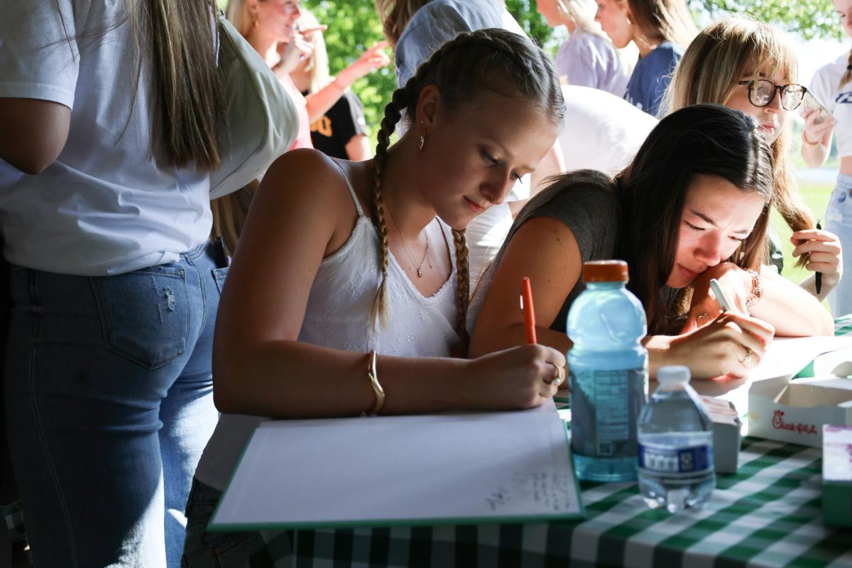 In the midst, Senior Mia LeFevre composes a note to put in her friend's yearbook during the senior picnic on May 9.