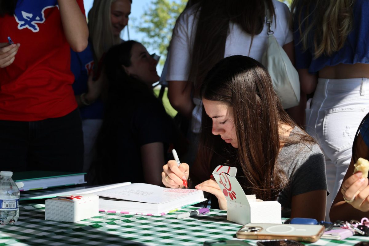 Pen in hand, senior Sophie Timmons writes a message to her classmate in her new yearbook at the senior picnic on May 9.