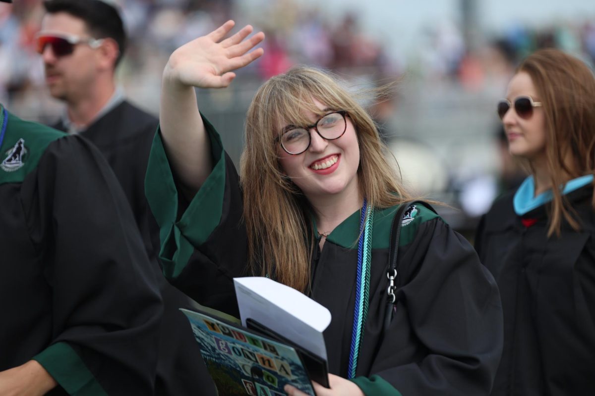 Waving, senior Maggie Roberts interacts with family and friends in the crowd after graduation. 