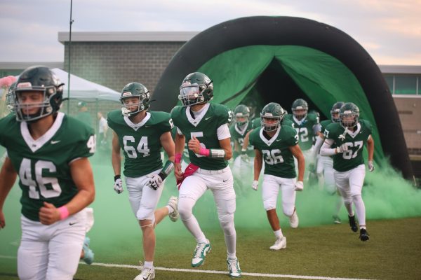 With the team, junior Max Orrick runs out of the tunnel before the football game against De Soto on Oct. 17.