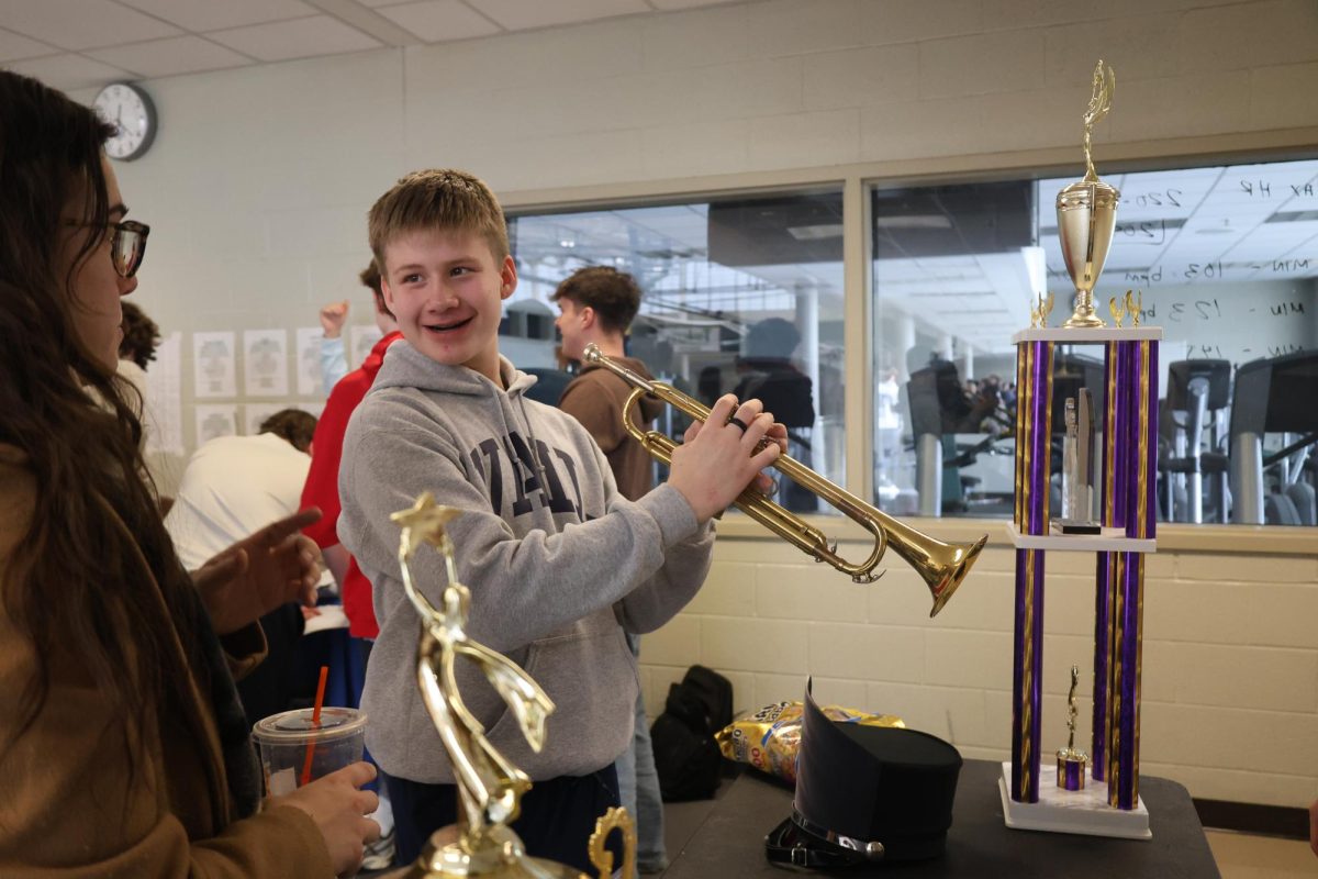 With a smile, freshman Damien Dunfee plays the trumpet at the band table during the enrollment fair on Jan. 15.