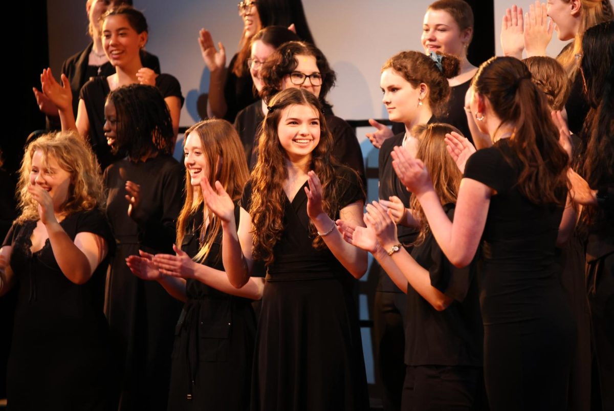 Clapping to the song, junior Isabel Buckingham smiles during a choir concert on March 26.