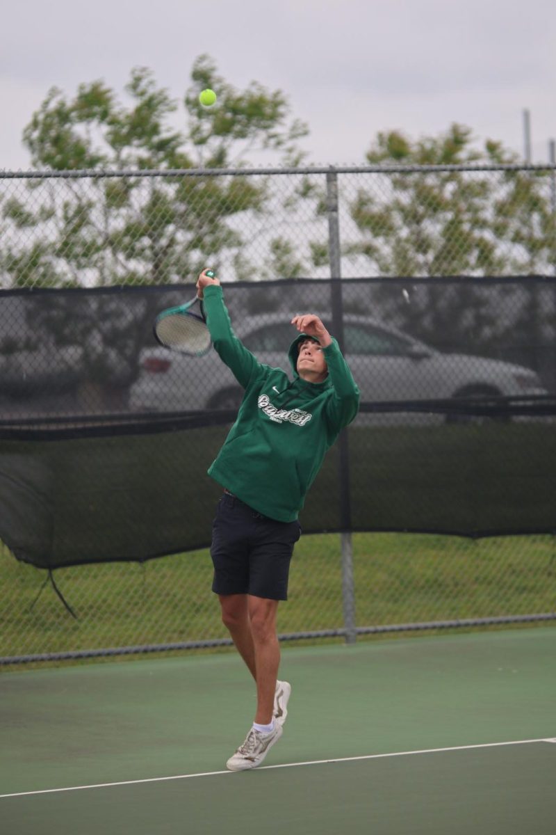 In focus, senior Wells Klusman completes a serve during his doubles match on April 23 against BVNW.