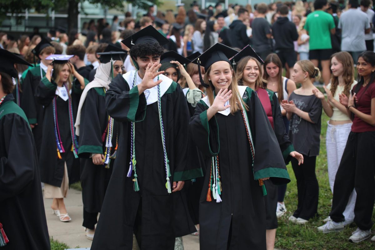 Waving, seniors Faraz Ahmadian and Erica Black walk through the courtyard before entering the gym for class day on May 15. The other grades lined up along the courtyard prior to the seniors walking through it.