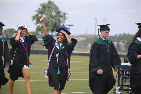 Waving, senior Joanna Suku smiles at the crowd as she walks into the ceremony.