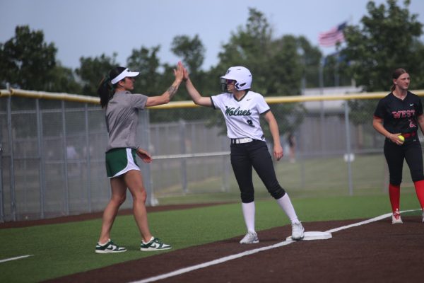 Celebrating, freshman Gabs Neilson high-fives her coach at the game against Blue Valley West on May 12.